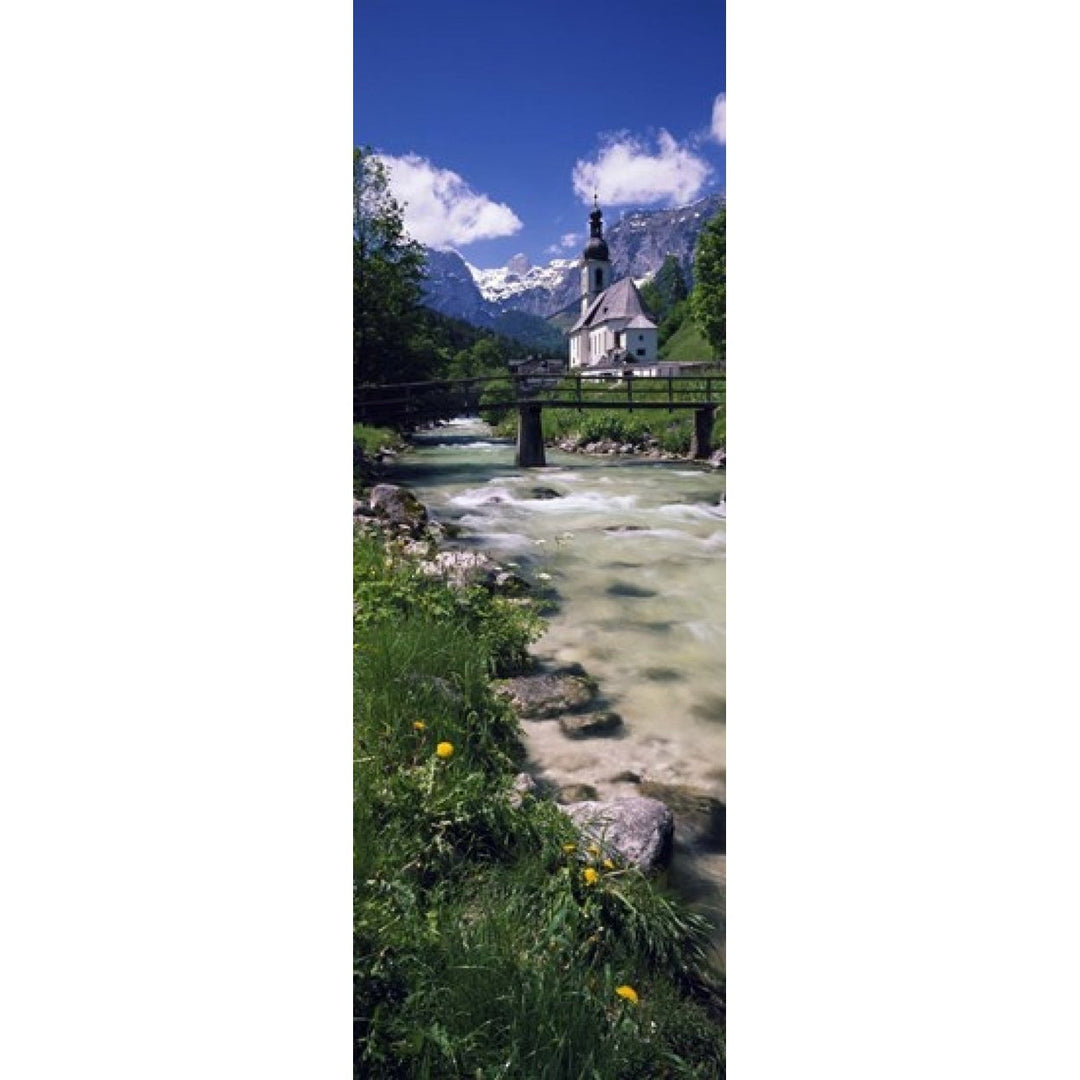 Bridge over stream below country church Bavarian Alps Germany. Poster Print (18 x 7) Image 1