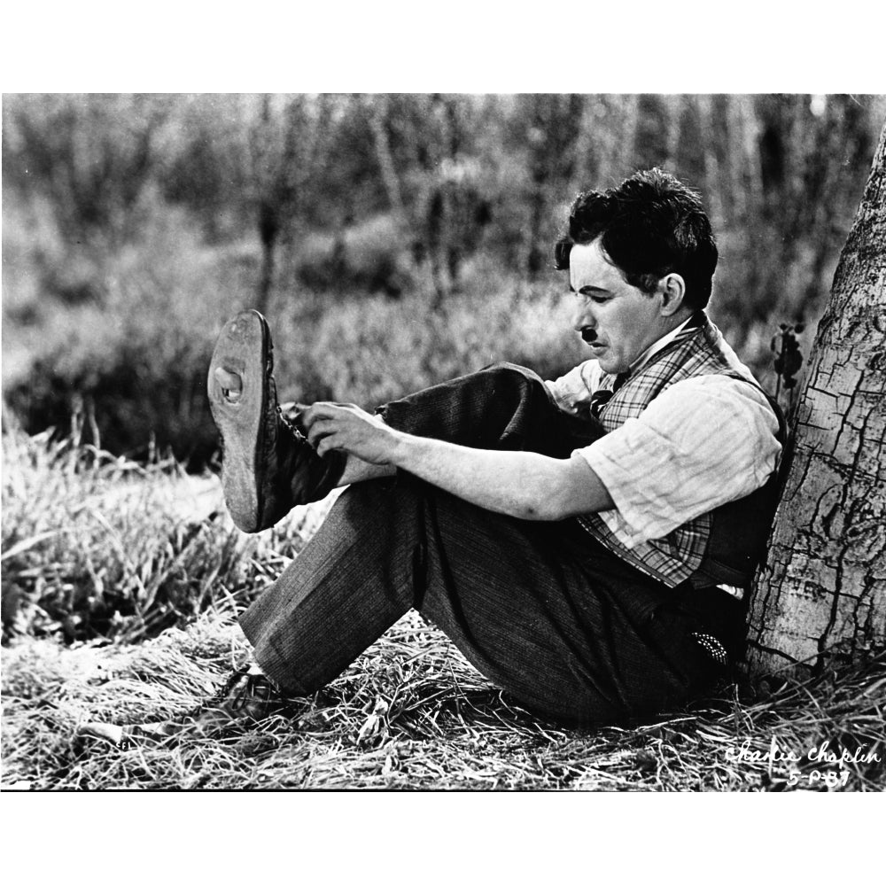 A film still of Charlie Chaplin putting on a shoe Photo Print Image 1