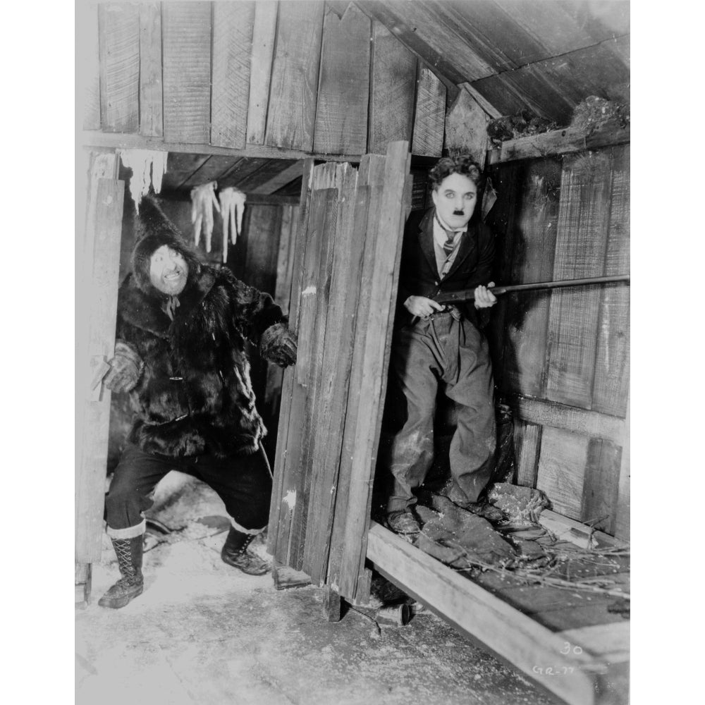 A film still of Charlie Chaplin hiding with a gun Photo Print Image 1