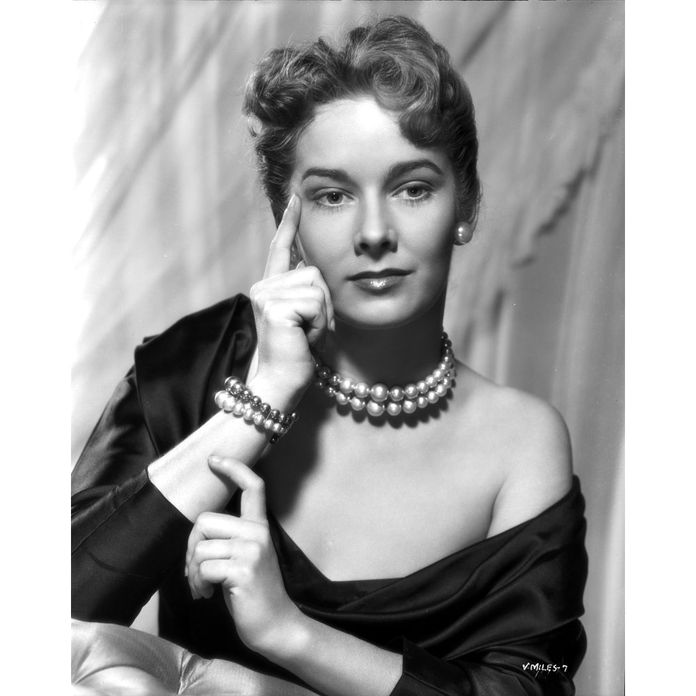 Vera Miles photographed waering a silk black off-the-shoulder boat neck gown with her finger pressed against her temple Image 1