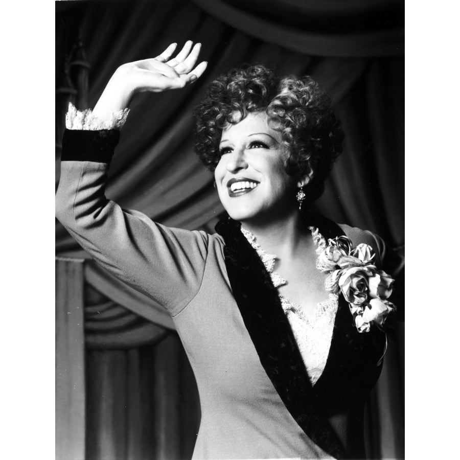 Bette Midler Portrait Waving Her Hand in Grey Linen Deep V-Neck Dress with White Ruffled Collar and Flower Corsage Photo Image 1