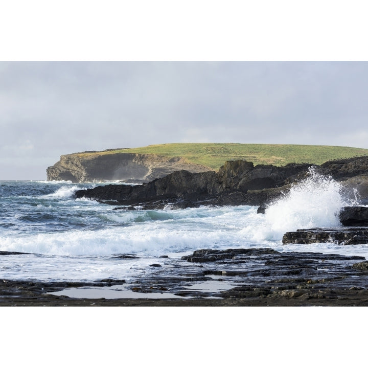 Waves crashing into rocky coast with large grassy hill and cliffs in background; Kilkee County Clare Ireland Image 1