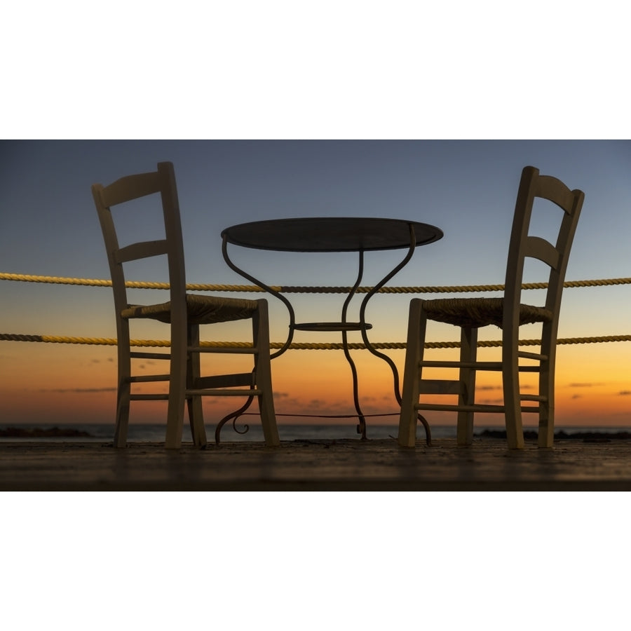 A table and chairs on a patio with a view of a colourful sunset; Paphos Cyprus Poster Print Image 1