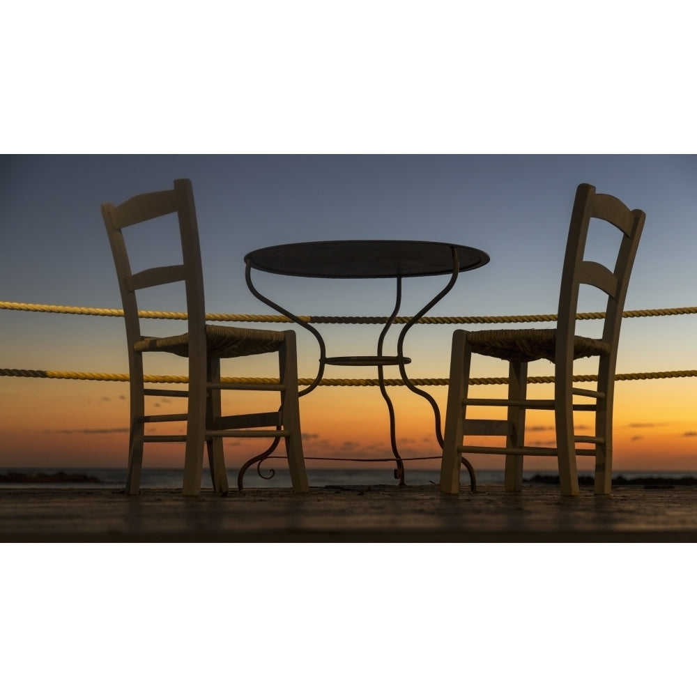 A table and chairs on a patio with a view of a colourful sunset; Paphos Cyprus Poster Print Image 2