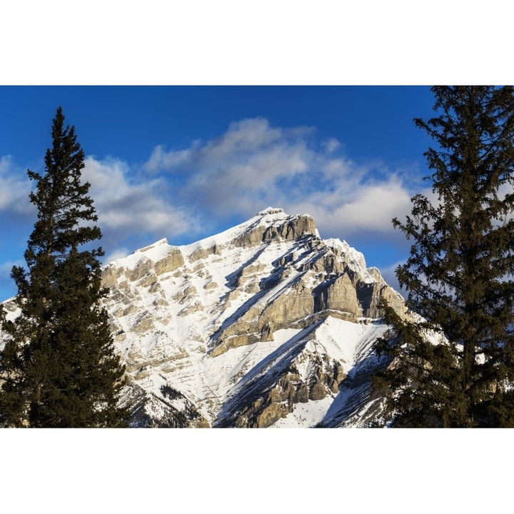 Snow covered mountain framed by evergreen trees with blue sky and clouds; Banff Alberta Canada Poster Print Image 1