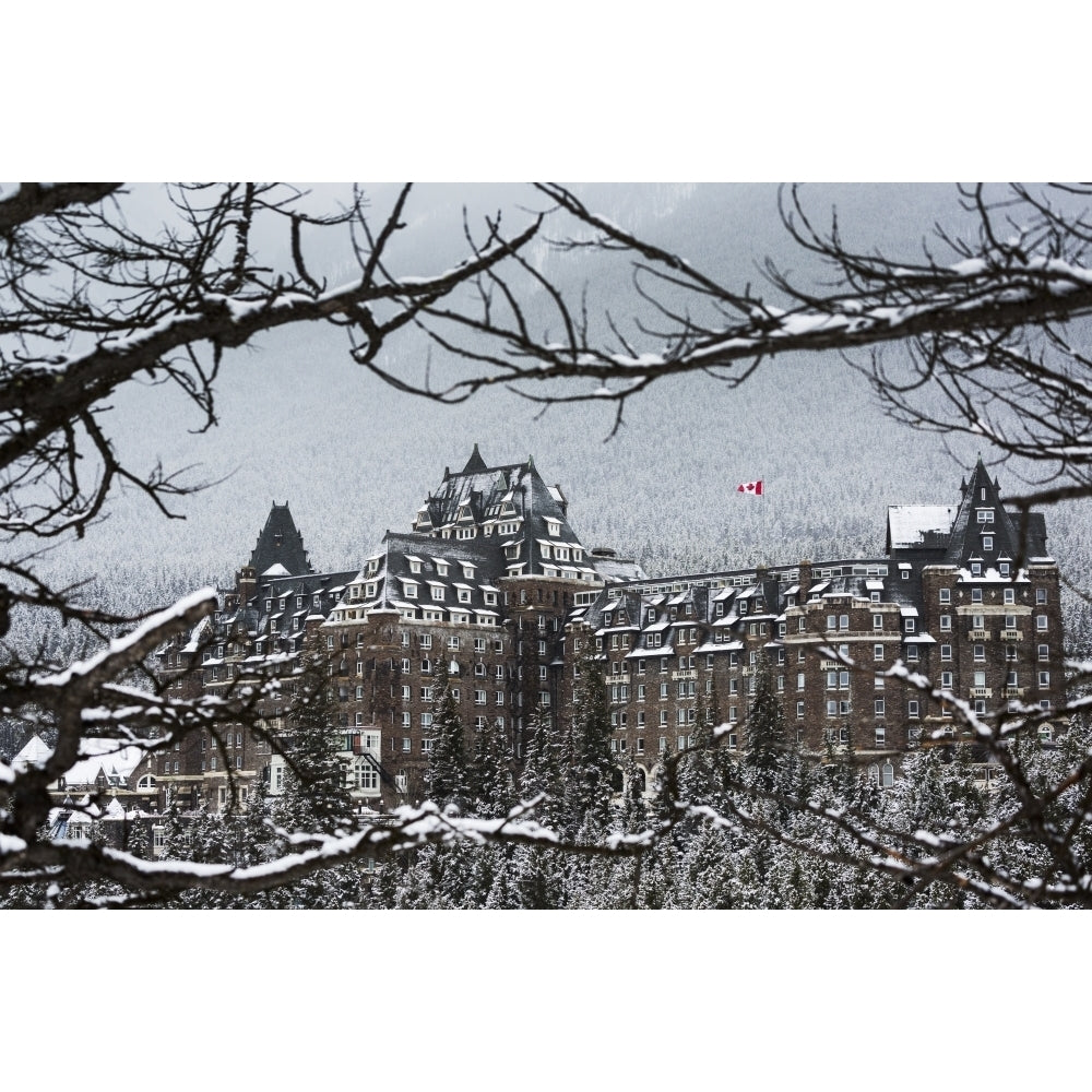 Snow covered Banff Springs Hotel framed by tree limbs with snow covered trees on mountain hillside in the background; Ba Image 2