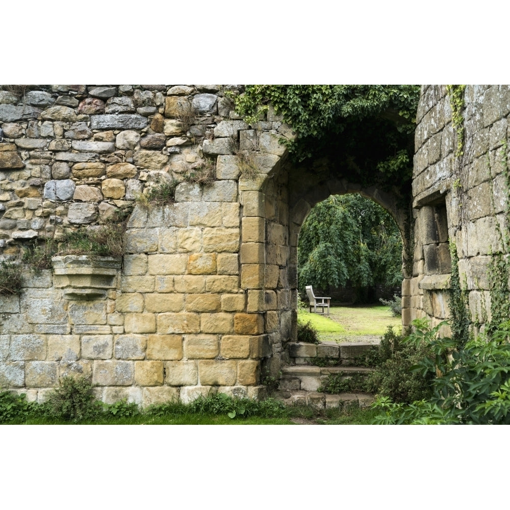 Stone wall overgrown with plants and steps up to a walkway Poster Print Image 1