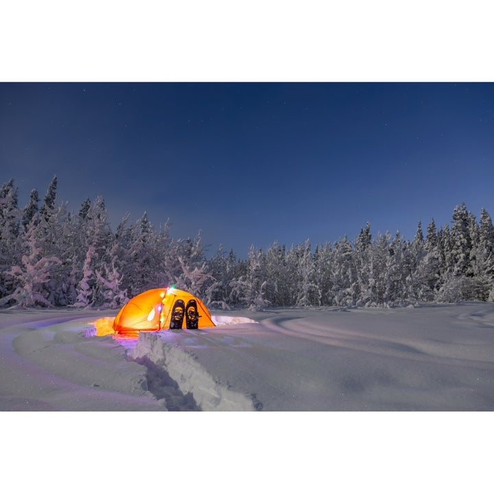 A glowing tent covered in string lights sits in the middle of an snowy spruce forest snowshoes in the deep snow outside Image 1