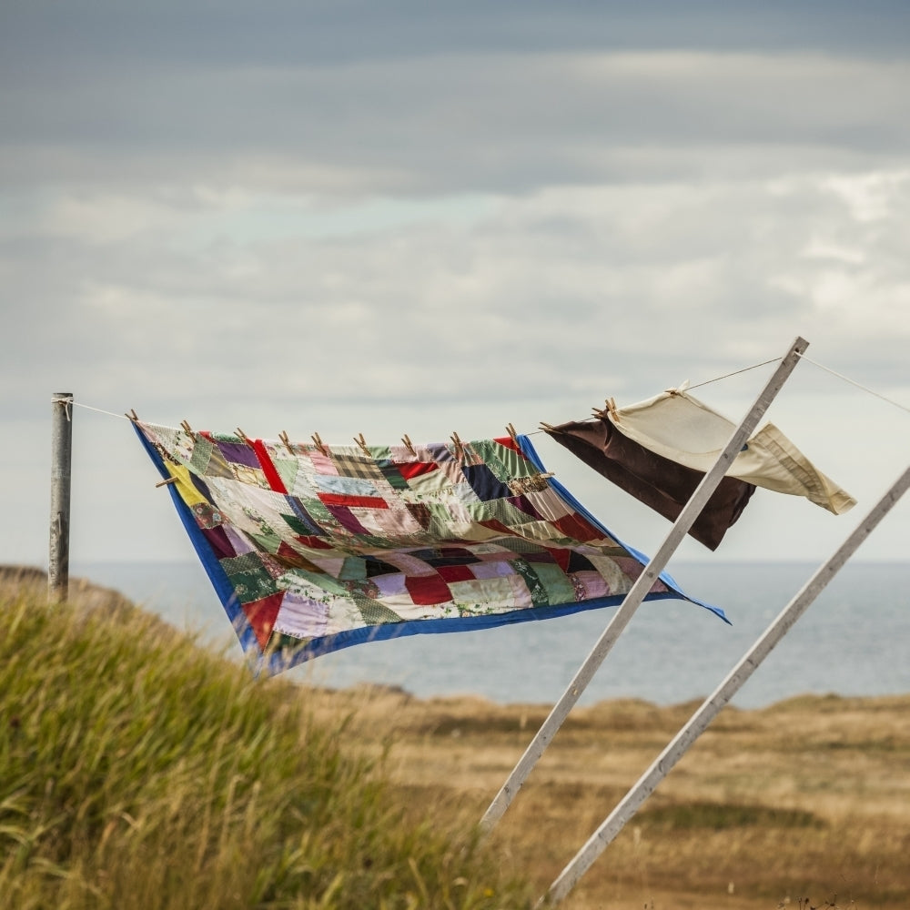 A patchwork blanket and pillow cases hanging on a clothesline with the Atlantic ocean in the background; Newfoundland Image 1