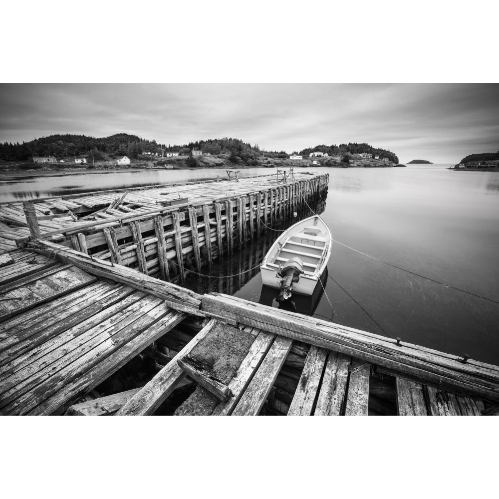 Black and white image of a boat tied to a wooden dock in a harbour along the Atlantic coast; Newfoundland Canada by Image 1