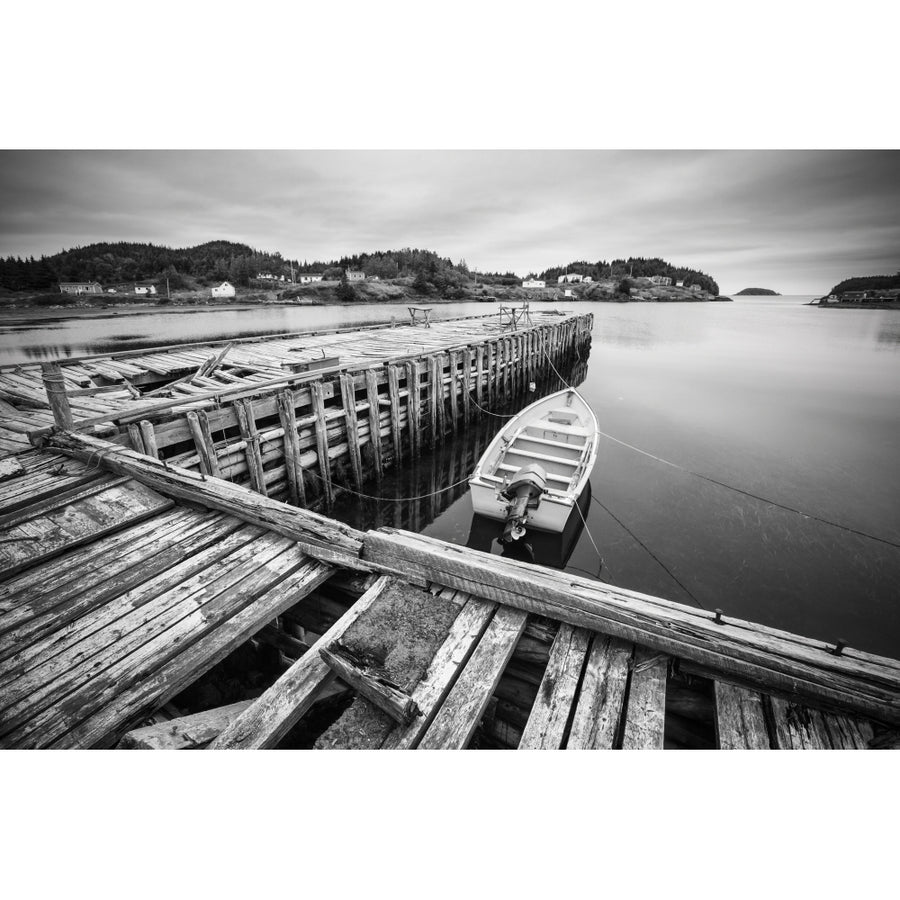 Black and white image of a boat tied to a wooden dock in a harbour along the Atlantic coast; Newfoundland Canada by Image 1