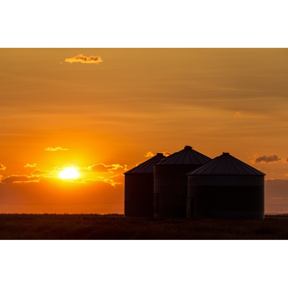 Silhouette of large metal grain bins at sunrise with orange sun rising over clouds; Alberta Canada by Michael Interisano Image 1