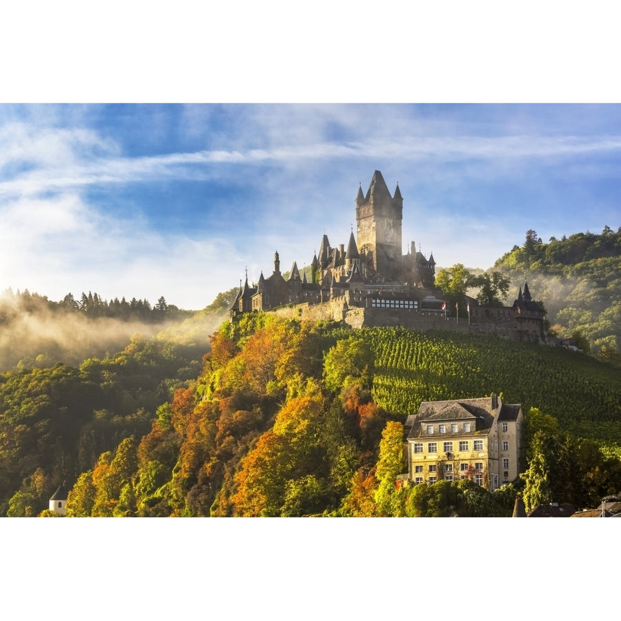 Large medieval castle on a colourful treed hillside with fog blue sky and cloud; Cochem Germany by Michael Interisano / Image 1