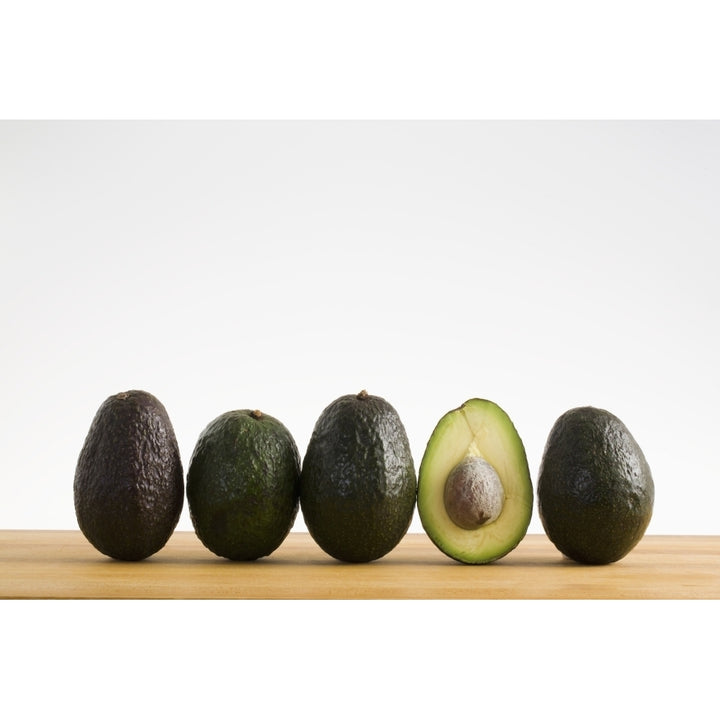 A Row Of Avocados Standing Upright On A Wooden Board With One Cut In Half With The Pit; Calgary Alberta Canada Image 1