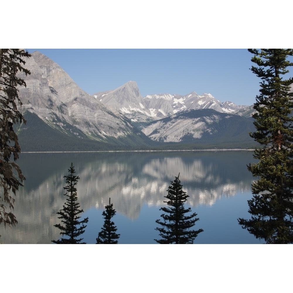 Mountain lake reflecting mountain range with snow and blue sky framed by trees in kananaskis provincial park;Alberta can Image 2