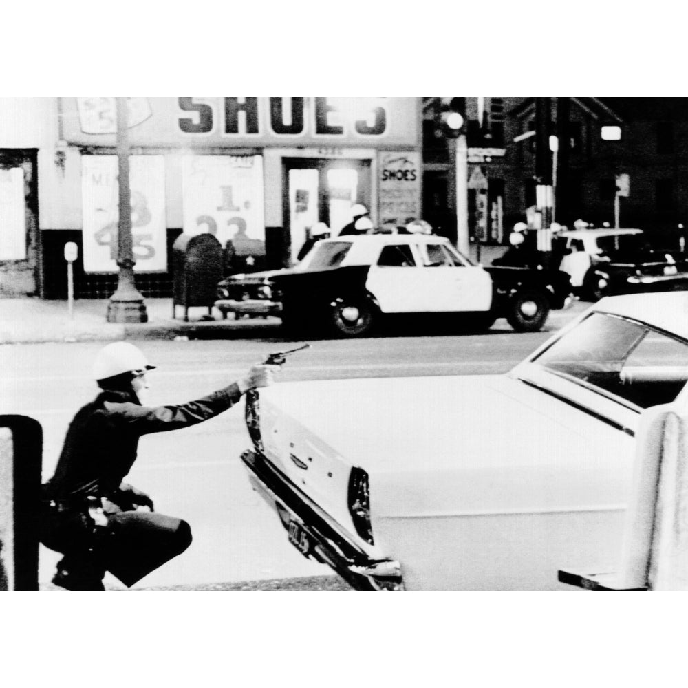 1965 Watts Riots. A Policeman Aims His Revolver At Building Where A Sniper Shot At Passing Cars. Across The Street Image 1