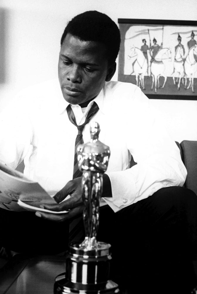 Sidney Poitier reading a newspaper with an Oscars statuette Photo Print Image 1