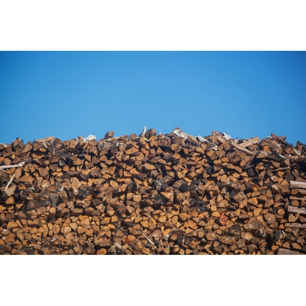 Stack of firewood pile against blue sky Poster Print Image 1