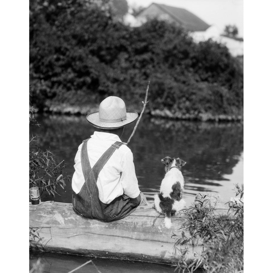 1920s-1930s Farm Boy Wearing Straw Hat And Overalls Sitting On Log With Spotted Dog Fishing In Pond Print By Vintage Image 1