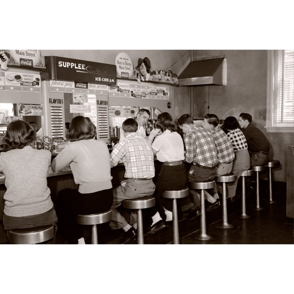 1950s Rear View Of Group Of Teenage Boys and Girls Sitting Together At A Soda Fountain Malt Shop Counter Snack Food Image 1