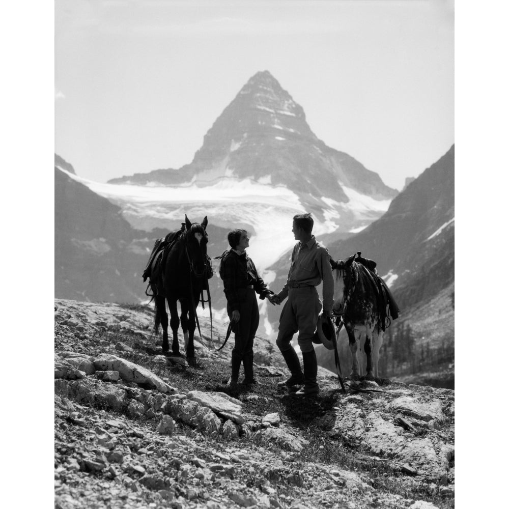 1920s-1930s Couple Man Woman Silhouetted Holding Hands Standing With Horses In Mountains Western Mt. Assiniboine Canada Image 1