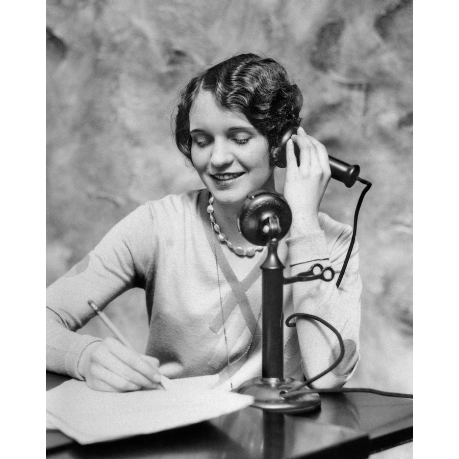 1920s Smiling Woman Sitting At Desk Writing And Talking On Candlestick Telephone Print By Vintage Collection Image 1