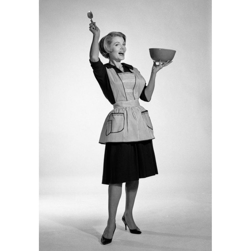 1960s Excited Woman Housewife In Apron Black Dress And High Heels Looking At Camera Holding Up Mixing Bowl And Kitchen Image 1