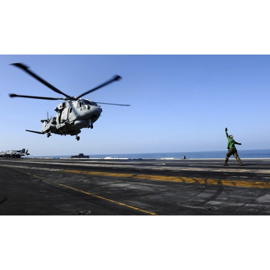 Airman directs an EH-101 Merlin helicopter onto the flight deck of USS John C. Stennis Poster Print Image 1