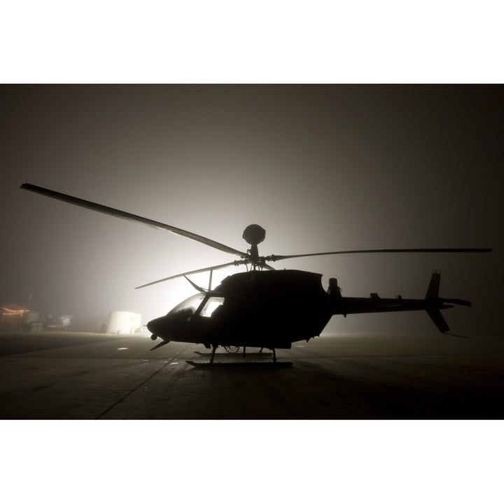 The illumination from the bright light silhouettes a OH-58D Kiowa helicopter during thick fog Poster Print Image 1