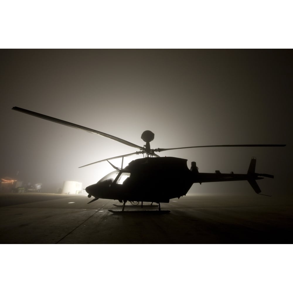 The illumination from the bright light silhouettes a OH-58D Kiowa helicopter during thick fog Poster Print Image 1