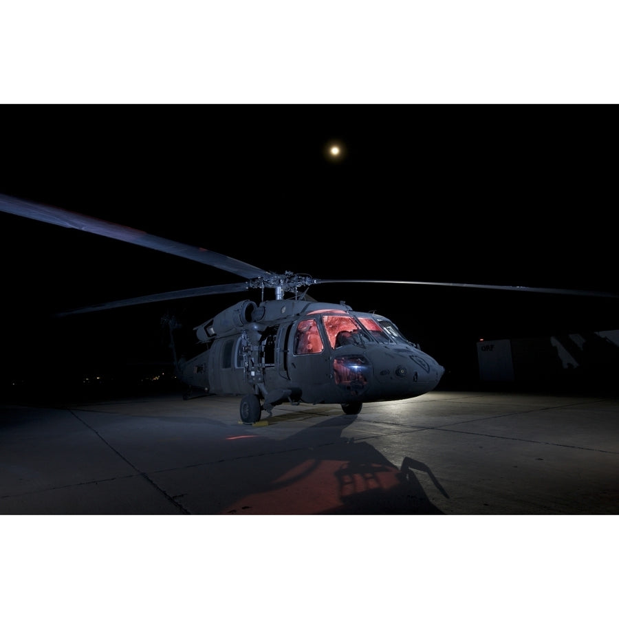 A UH-60 Black Hawk helicopter parked on the flight line under a full moon Poster Print Image 1