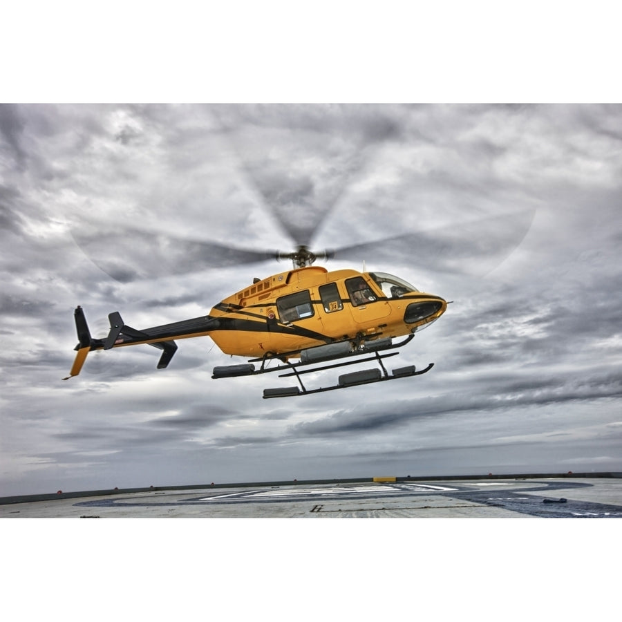 A Bell 407 utility helicopter prepares to land on an oil rig Poster Print Image 1