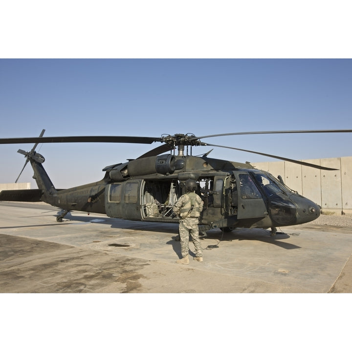 A U.S. Army crew chief stands next to a UH-60 Black Hawk Poster Print Image 1