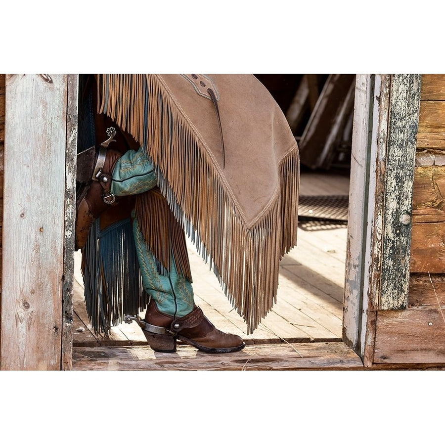 USA- Shell- Wyoming. Hideout Ranch cowgirl standing in doorway with cowboy boots and chaps. Poster Print - Darrell Image 1